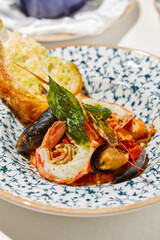 Seafood platter with cooked shrimps, mussels, sea scallops in tomato sauce on white table. Stew seafood in italian style with ciabatta bread. Seafood dish: prawns, shellfish, scallops on ceramic plate