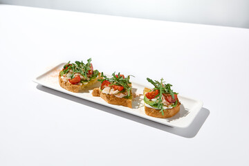 Aesthetic composition with shrimp bruschetta on white background over white wall. Italian bruschetta with shrimp, tomatoes and arugula on fine dining in summer. Elegant menu concept.