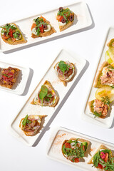 Aesthetic composition with bruschetta on white background over white wall. Set of bruschetta with shrimp, salmon, beef, tomatoes and crab on fine dining in summer. Elegant menu concept.