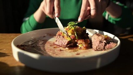 A girl cuts a steak on a plate with a fork and a knife, close-up. Dinner in a restaurant