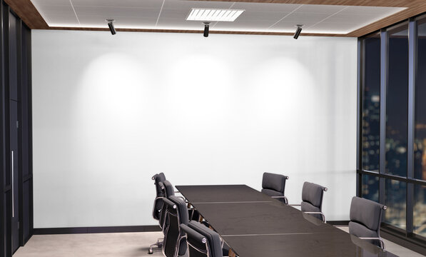 Blank White Wall Mockup In Dark Modern Office With Windows And Spotlights. Empty Company Meeting Room 3D Rendering