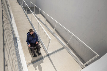 Man on wheelchair, approaching the building moving along an accessible ramp for persons with disability