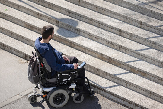 Person with disability on electric wheelchair stopping at the bottom of inaccessible staircase, unable to reach the top