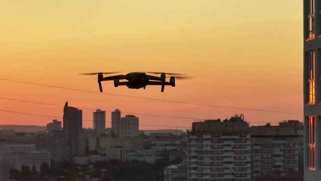 Silhouette of drone in flight at slow speed over the city at summer sunset. Close up drone view.