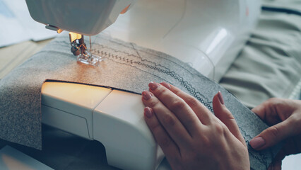 Close-up shot of working modern sewing machine, fabric and manicured female hand. Clothes...