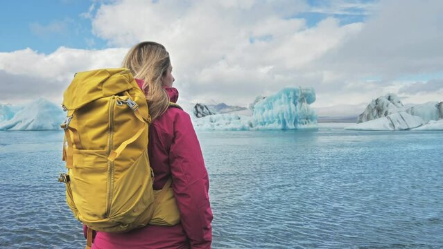 woman hiker wearing backpack standing in front of jokulsarlon  lagoon,iceberg glacier lake,female traveller excursionist looking icebergs floating drifting sea water,vatnajokull national park iceland