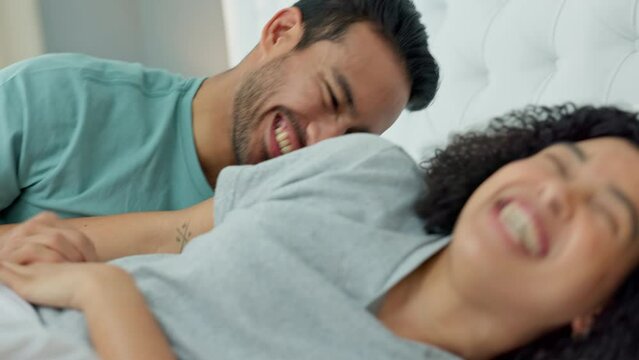 Bedroom fun, laugh and silly couple lying in bed and being playing and enjoying free time together. Man tickling and teasing woman while enjoying lazy morning, honeymoon love and weekend at home