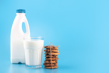 Tasty cocoa cookies with chocolate drops. A bottle and a glass of milk isolated on blue background. flatlay, text space.