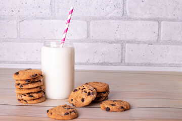 Glasses of fresh milk with straw and brown school chocolate cookies. The cookies with chocolate drops and on a rustic wood kitchen table, with copy space. yummy and tasty