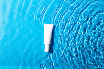 Mock up white tube with cosmetic product for moisturizing in water on blue background. Template for design.