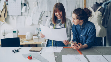 Attractive young women working in design industry are comparing sketches and talking about them...