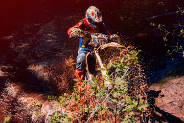 motorcycle racer on an enduro sports motorcycle crosses a river in a ford in an off-road race in summer on a sunny day