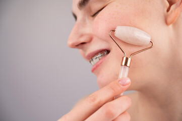 Close-up portrait of a woman uses a quartz roller massager to smooth wrinkles on her forehead.