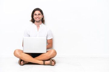 Young handsome man with a laptop sitting on the floor isolated on white background keeping the arms crossed in frontal position