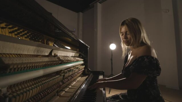 Pianist playing upright piano with open sound board showing hammers striking the strings