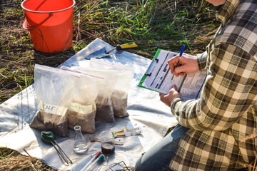 Male agronomist preparing soil samples in sample bags for laboratory analysis, writing in...