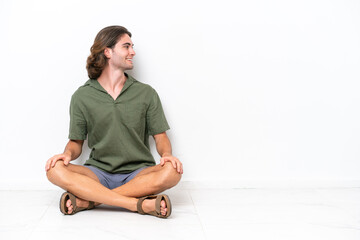 Young handsome man sitting on the floor isolated on white background in lateral position