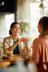 Happy Asian entrepreneur talks to her colleague during coffee break in cafe. - obrazy, fototapety, plakaty