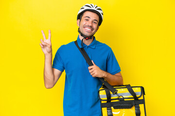 Young handsome man with thermal backpack over isolated yellow background smiling and showing victory sign