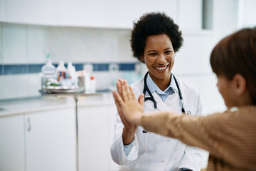 Happy African American pediatrician gives high five to kid after medical examination at doctor's...