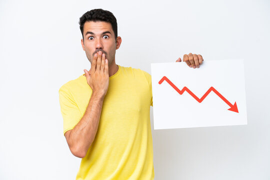 Young handsome man over isolated white background holding a sign with a decreasing statistics arrow symbol with surprised expression