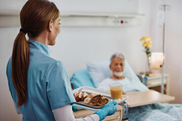 Caring nurse serving meal to patient who is recovering in hospital ward.
