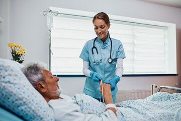 Happy nurse putting pulse oximeter on senior patient's finger during his recovery at intensive care...