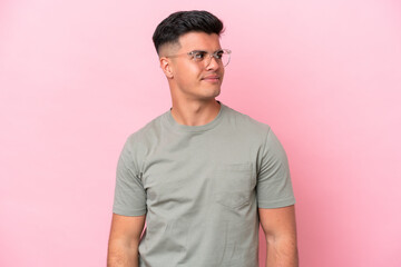 Young caucasian handsome man isolated on pink background having doubts while looking side
