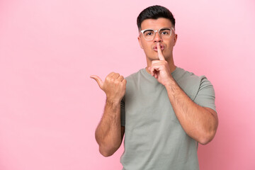 Young caucasian handsome man isolated on pink background pointing to the side and doing silence gesture