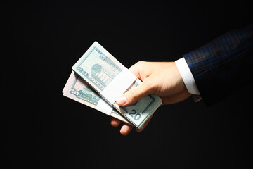 Concept of financials, businessman hand holds dollars on dark background
