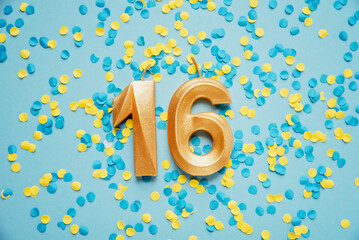 Number 16 sixteen golden celebration birthday candle on yellow and blue confetti Background. sixteen years birthday. concept of celebrating birthday, anniversary, important date, holiday