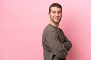Young caucasian man isolated on pink background with arms crossed and happy