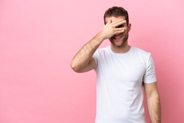 Young caucasian man isolated on pink background covering eyes by hands and smiling