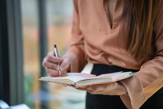 Cropped image of a businesswoman's hand is taking notes while standing in an office