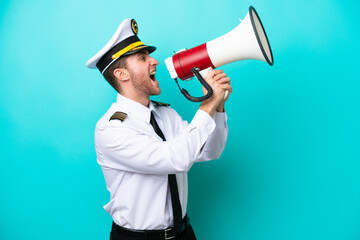 Airplane caucasian pilot isolated on blue background shouting through a megaphone