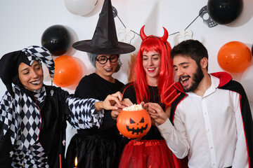 Four people eating popcorn from a pumpkin at a costume Halloween party in a house.