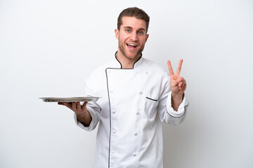 Young caucasian chef with tray isolated on white background smiling and showing victory sign