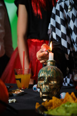 Woman lights a candle on a skull with a lighter at a costume Halloween party.