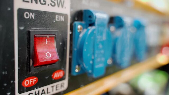 Close-up red button on the background of the blue power sockets of the gas generator. The finger starts the electric gas generator by pressing the red switch. Restoration of autonomous power supply
