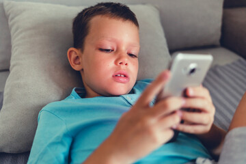 Little boy on cell phone. Teenager chatting with friends on smartphone lying on couch, social network.