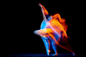 Young and graceful female ballet dancer dancing over dark background in mixed neon light. Art, motion, action, flexibility, inspiration concept.