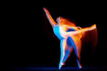 Young and graceful female ballet dancer dancing over dark background in mixed neon light. Art, motion, action, flexibility, inspiration concept.