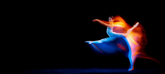 Ease of movement. Tender female ballet dancer dancing solo dance over dark background in mixed neon...