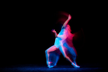 Graceful ballerina dancing on dark background in mixed neon light. Grace, movement, action and motion concept. Looks weightless, flexible. © master1305