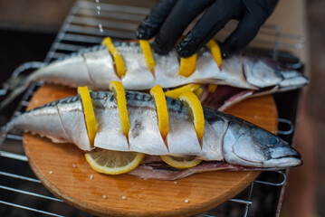 Fish (mackerel) with lemon. Chef in a black latex gloves prepares mackerel fish on a wooden cutting...