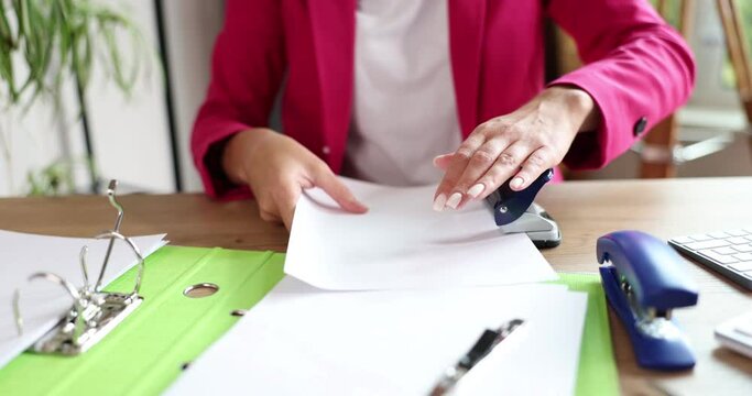 Closeup of female hands punching holes using documents in office