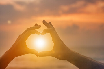 Silhouette hands of woman and man are lovely heart shape with sunset on through hand. Couple hands in heart shape with sunrise in middle and sea (ocean) background. Togetherness and love. Copy space