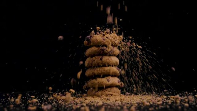 Stack of vegan chocolate cookies with biscuit crumbs falling on them while they rotate, slow motion, black background, static shot