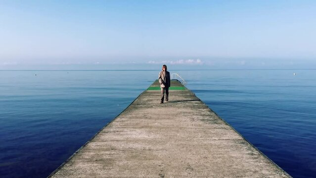Businesswoman walks to sea at old abandoned pier in fashion style business classic costume. High quality 4k raw footage