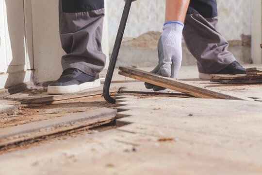 Home improvement. Construction worker or handyman is removing old wooden parquet flooring using crowbar tool. Old wooden floor renovation.